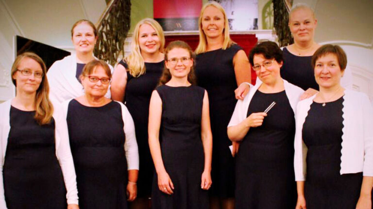 Yhdeksän naista seisoo kahdessa rivissä Milavidan aulassa portailla. Naiset ovat pukeutuneet mustiin mekkoihin ja valkoiseen jakkuun.