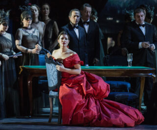 A woman in a ded dress is sitting on a sofa on stage.