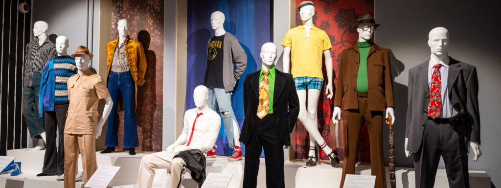 Miesten muotia eri vuosikymmeniltä museon korokkeella mallinukkejen päällä.