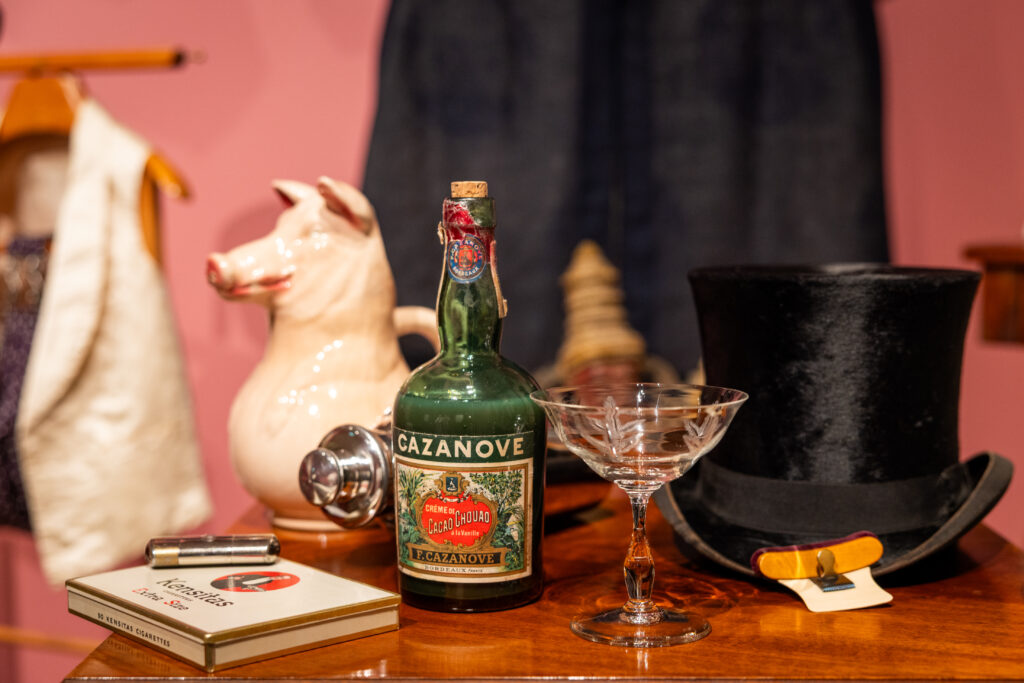 Keikarin esineistöä museon näyttelyssä. Pöydällä on muun muassa silinterihattu, pullo, lasi ja sikarirasia.